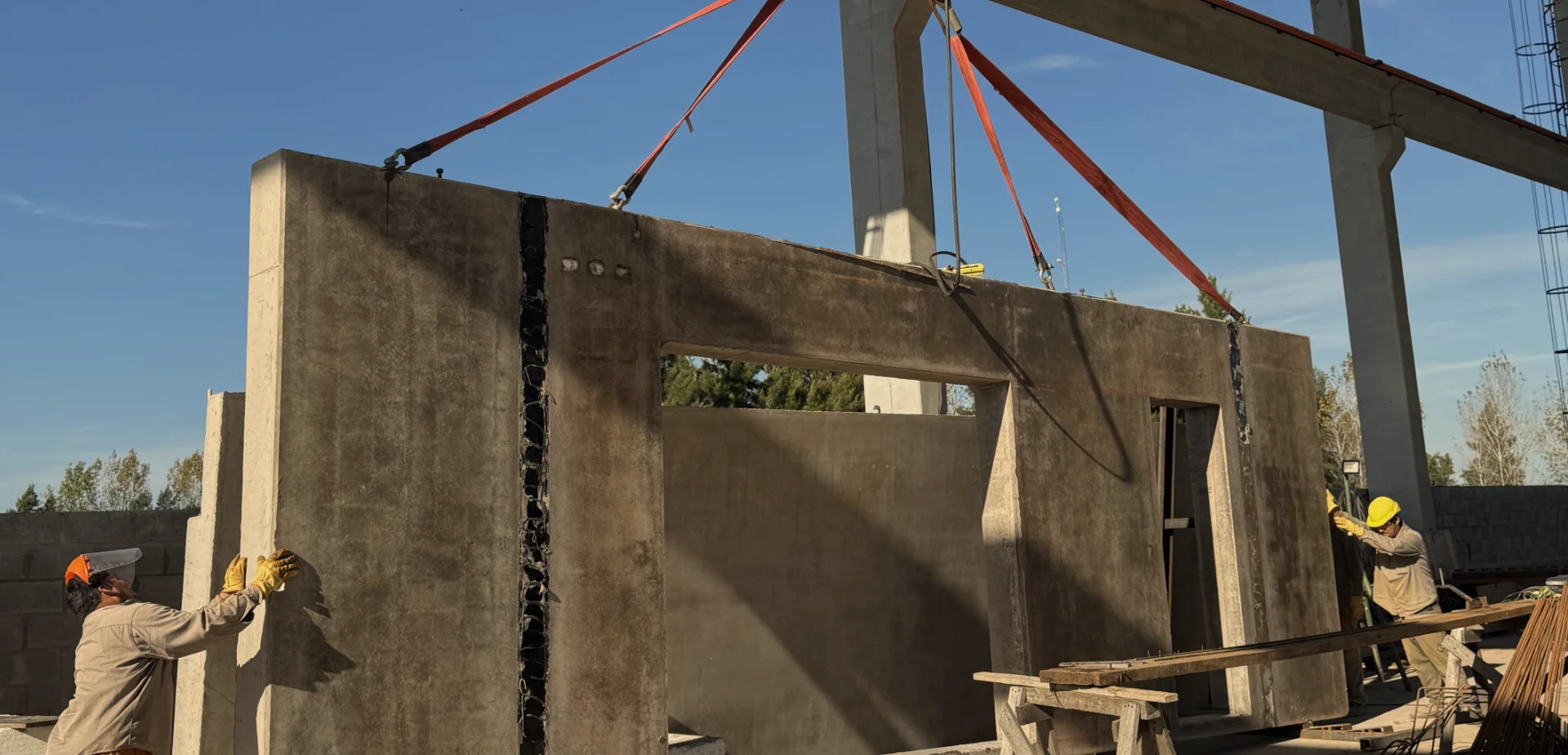 Operarios de construcción guiando el montaje de un panel de hormigón con grúa.